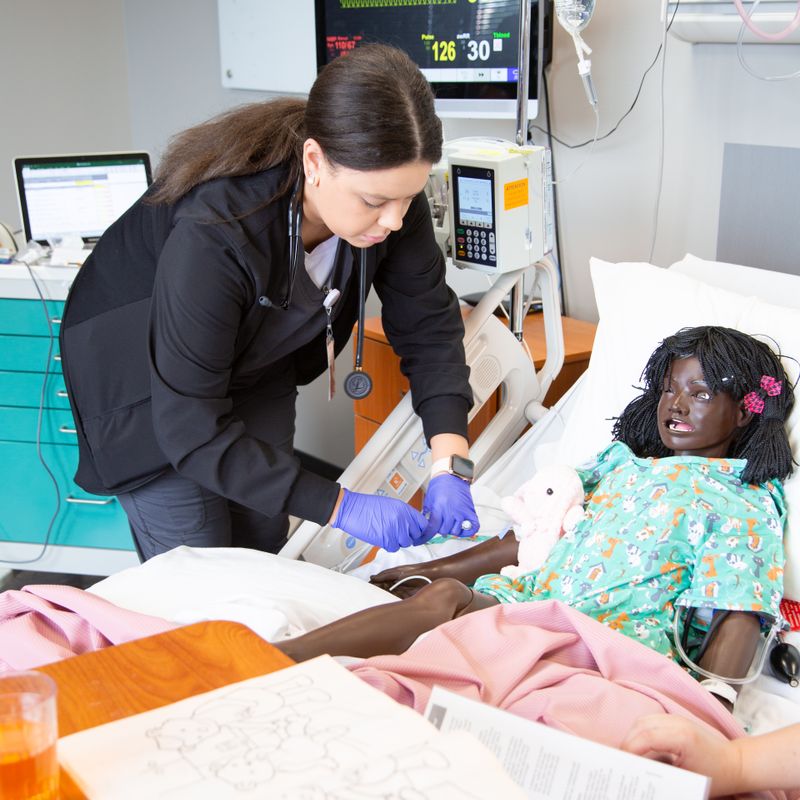 Student administering medicine to simulation doll